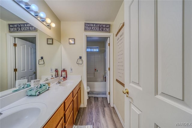 bathroom with double vanity, toilet, wood finished floors,  shower combination, and a sink