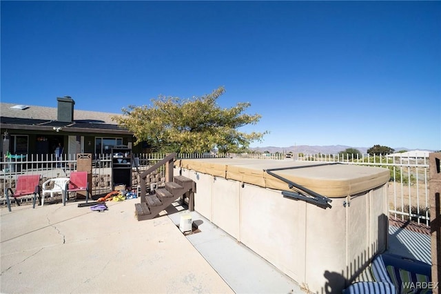 view of patio featuring fence, a mountain view, and a hot tub