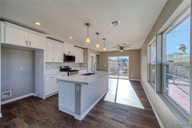 kitchen with a center island with sink, hanging light fixtures, white cabinetry, a sink, and stainless steel gas range oven