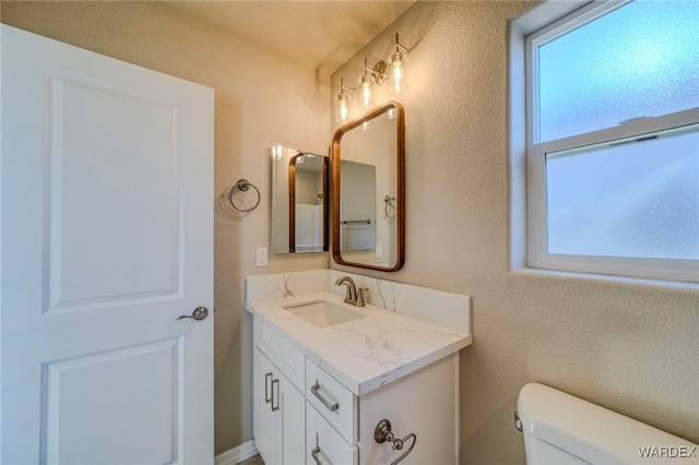 bathroom with toilet, a textured wall, and vanity