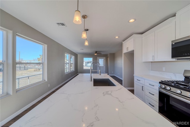 kitchen with visible vents, appliances with stainless steel finishes, hanging light fixtures, light stone countertops, and a sink