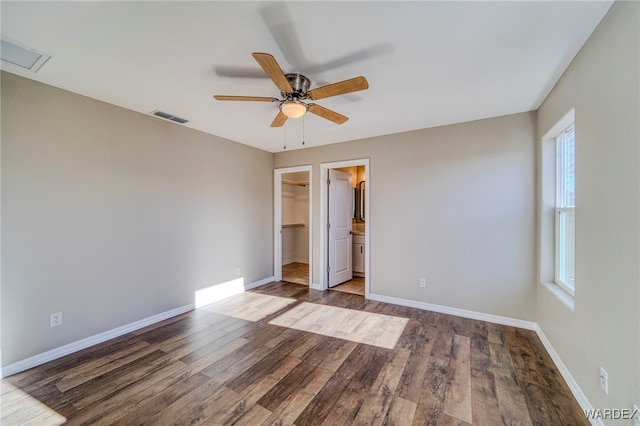 unfurnished bedroom featuring a walk in closet, baseboards, visible vents, and dark wood finished floors