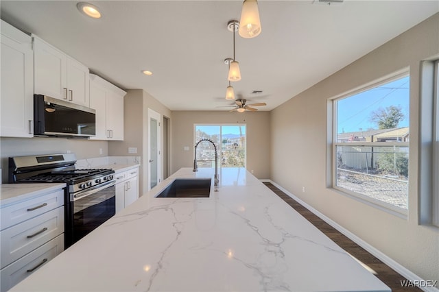 kitchen with white cabinets, hanging light fixtures, light stone countertops, stainless steel appliances, and a sink