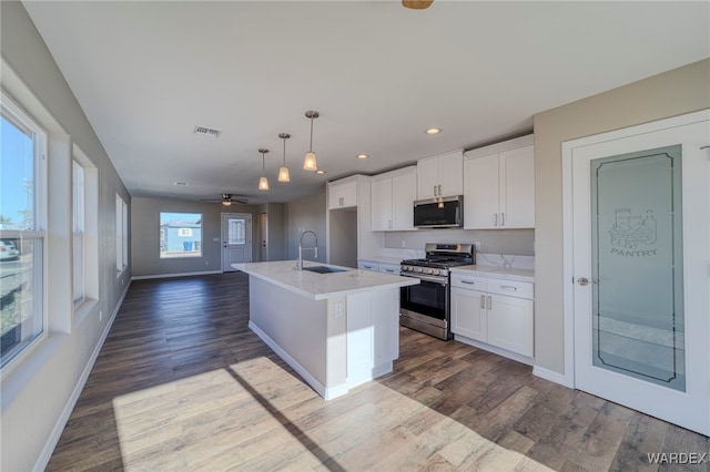 kitchen with stainless steel appliances, a sink, white cabinetry, an island with sink, and pendant lighting