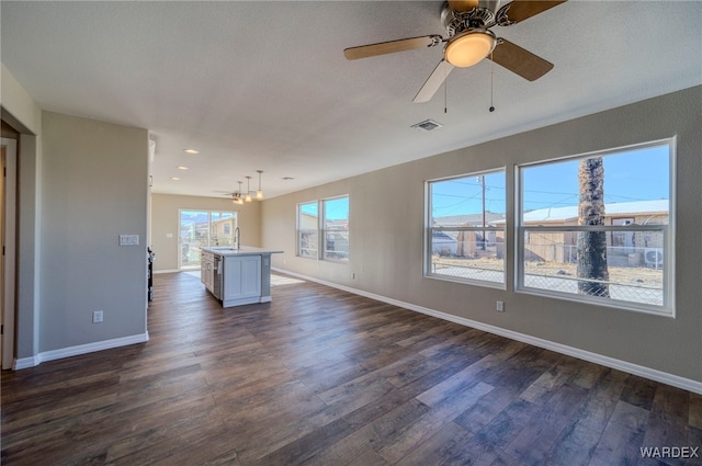 unfurnished living room with baseboards, visible vents, a ceiling fan, dark wood-style flooring, and a sink