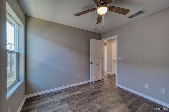 empty room featuring dark wood-type flooring, visible vents, baseboards, and a ceiling fan