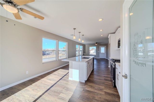 kitchen with decorative light fixtures, light countertops, white cabinetry, an island with sink, and stainless steel gas range oven