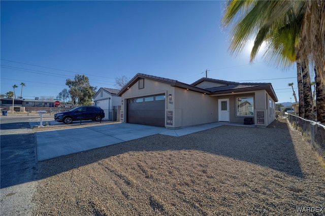 ranch-style home with driveway, an attached garage, fence, and stucco siding