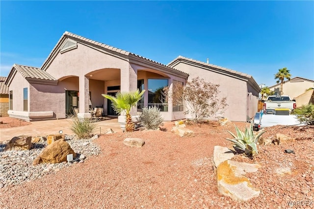 rear view of property featuring a patio, a tiled roof, and stucco siding