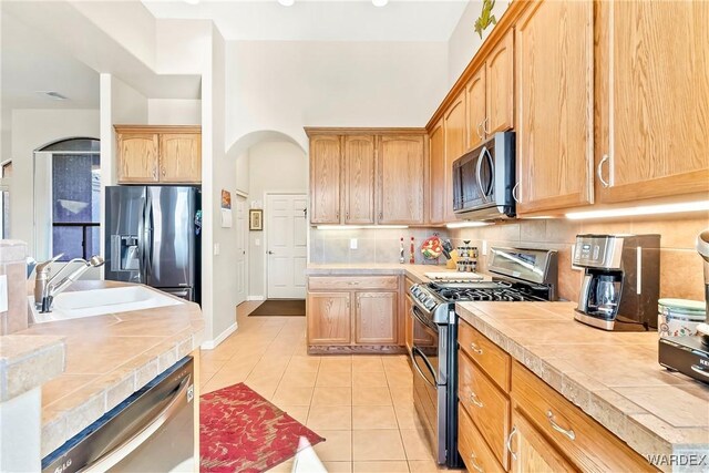 kitchen featuring light tile patterned floors, tile countertops, stainless steel appliances, a sink, and decorative backsplash