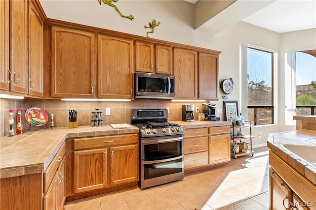 kitchen featuring appliances with stainless steel finishes, tile counters, brown cabinetry, and backsplash