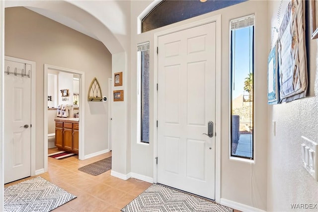 foyer with arched walkways, baseboards, and light tile patterned floors