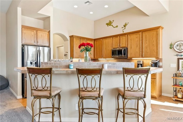 kitchen with light tile patterned floors, tasteful backsplash, visible vents, a breakfast bar, and stainless steel appliances