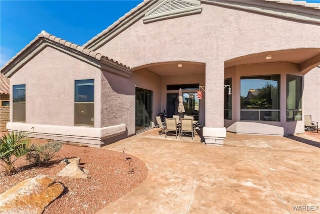 rear view of house with a patio, outdoor dining area, a tiled roof, and stucco siding