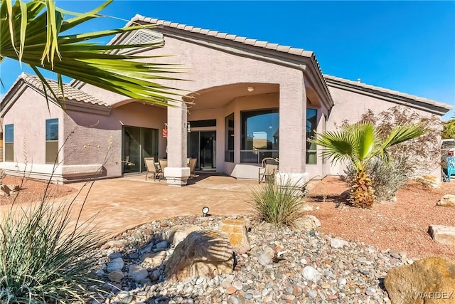 rear view of property with a patio, a tiled roof, and stucco siding