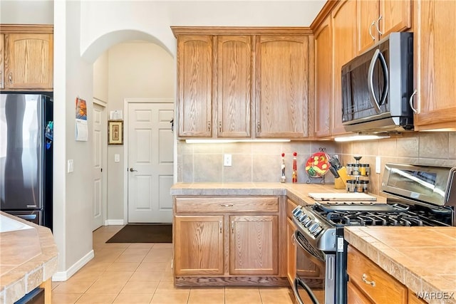 kitchen with arched walkways, tile countertops, light tile patterned flooring, stainless steel appliances, and tasteful backsplash