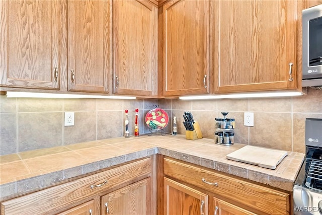 kitchen featuring tile counters, stainless steel microwave, and backsplash