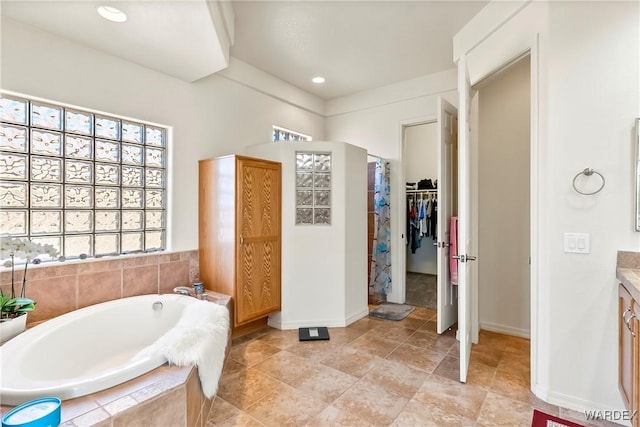 full bath with a walk in closet, recessed lighting, vanity, baseboards, and a bath