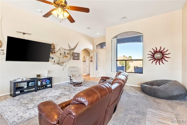 carpeted living area with arched walkways, ceiling fan, visible vents, and baseboards