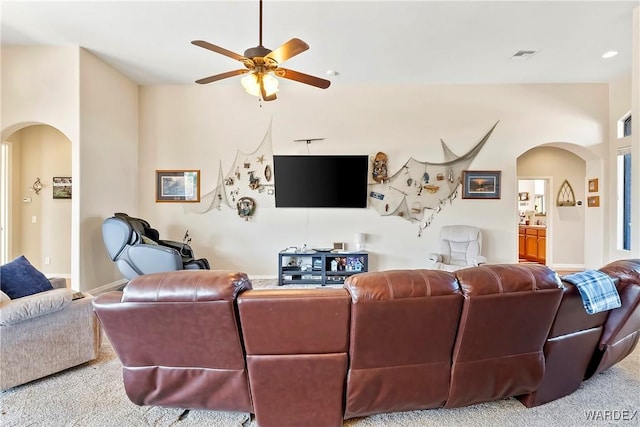 living room featuring ceiling fan, visible vents, arched walkways, and light colored carpet