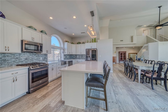 kitchen with decorative light fixtures, light countertops, appliances with stainless steel finishes, white cabinets, and a kitchen island