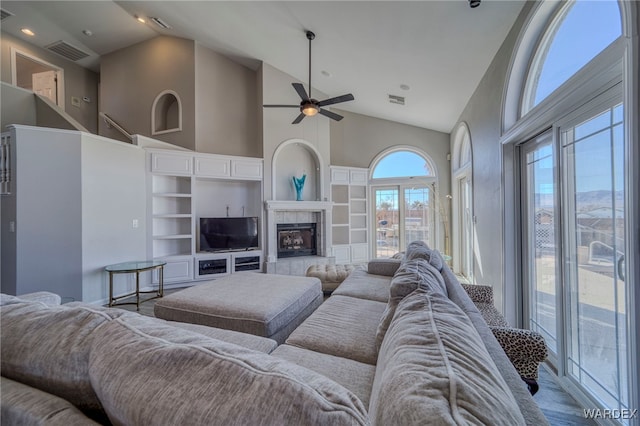 living room with high vaulted ceiling, ceiling fan, visible vents, and a tiled fireplace