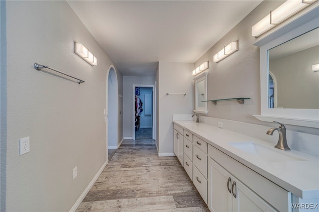 bathroom featuring double vanity, baseboards, a sink, and wood finished floors