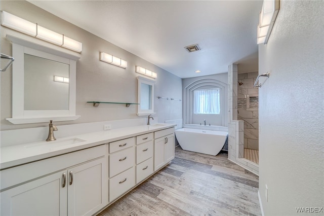 bathroom featuring a tile shower, wood finished floors, a sink, and visible vents