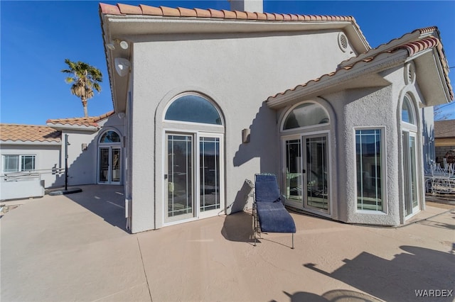 rear view of house with a patio, a tiled roof, and stucco siding