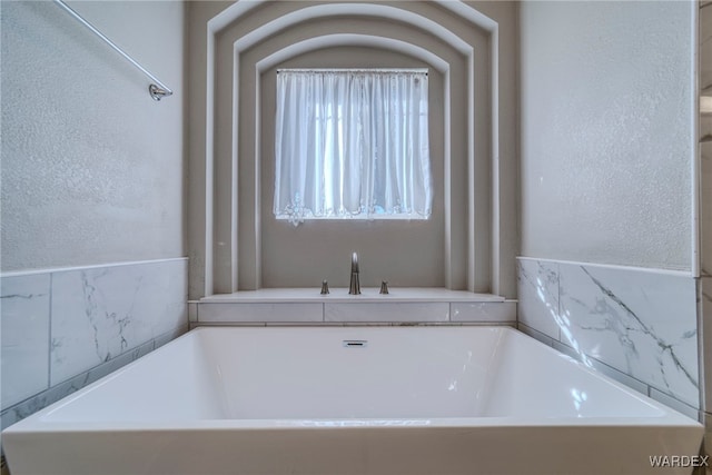 full bath with a textured wall and a freestanding tub