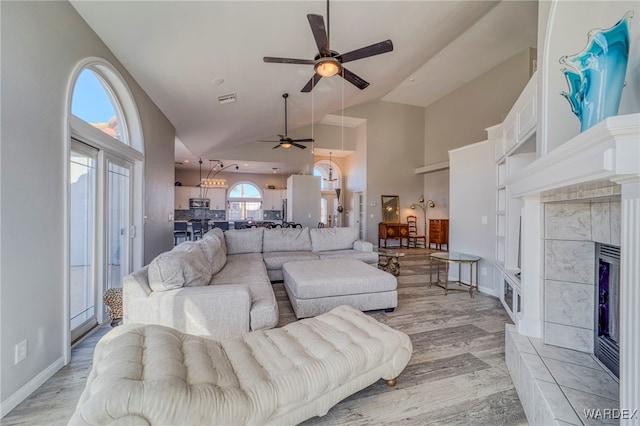 living room featuring visible vents, a tiled fireplace, high vaulted ceiling, light wood-type flooring, and baseboards