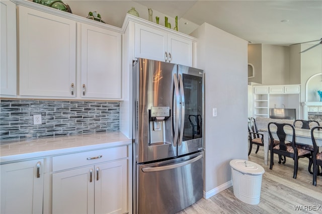 kitchen featuring white cabinets, light countertops, light wood-type flooring, decorative backsplash, and stainless steel fridge