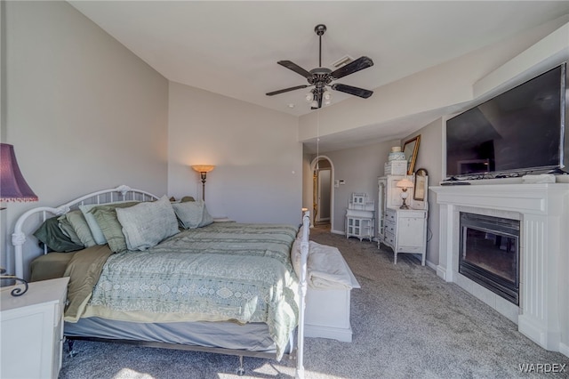 bedroom featuring baseboards, arched walkways, a glass covered fireplace, ceiling fan, and carpet flooring