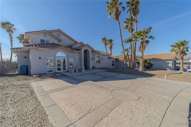 mediterranean / spanish-style home featuring stucco siding, a tile roof, fence, and french doors