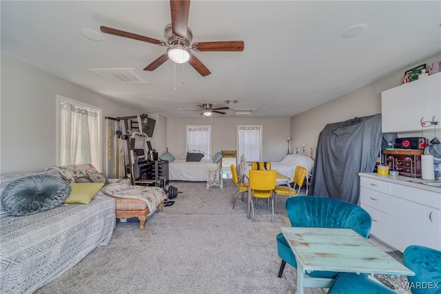 interior space featuring ceiling fan, multiple windows, visible vents, and light colored carpet