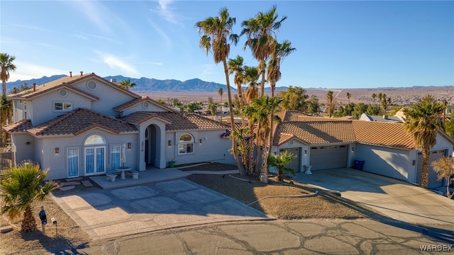 mediterranean / spanish-style home featuring a tile roof, stucco siding, an attached garage, a mountain view, and driveway