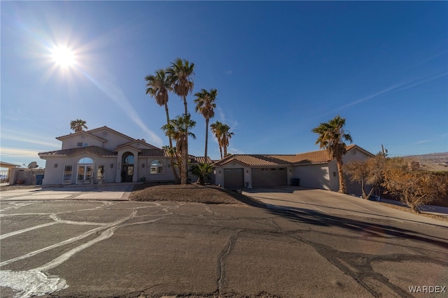 mediterranean / spanish-style home with a tile roof, driveway, an attached garage, and stucco siding