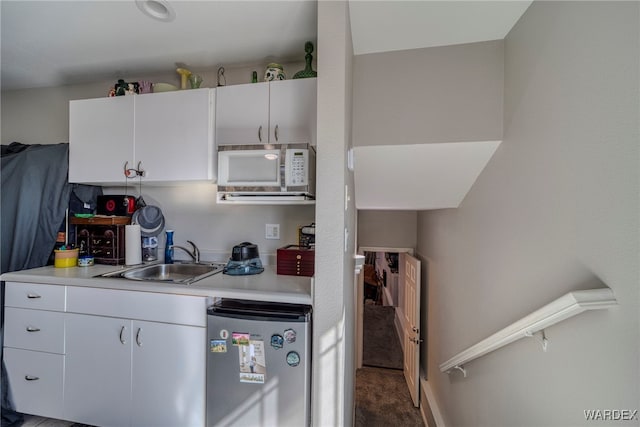 kitchen featuring white cabinets, freestanding refrigerator, light countertops, dark carpet, and a sink