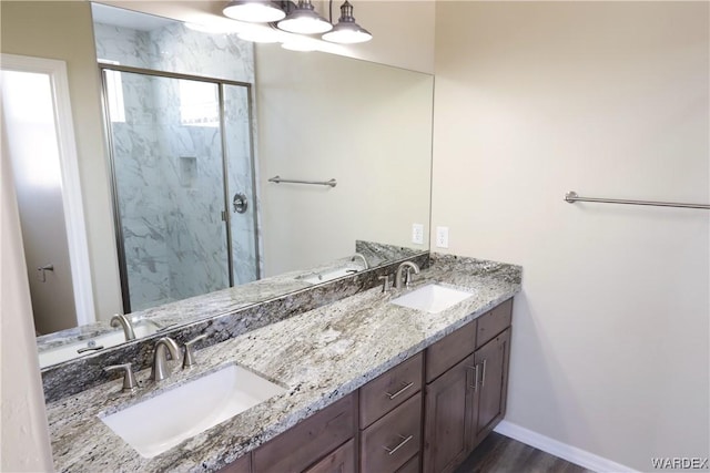 full bathroom featuring baseboards, a sink, a marble finish shower, and double vanity