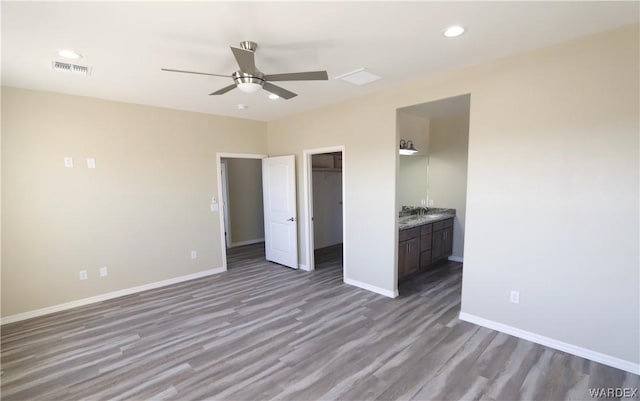 unfurnished bedroom with baseboards, visible vents, wood finished floors, a walk in closet, and recessed lighting