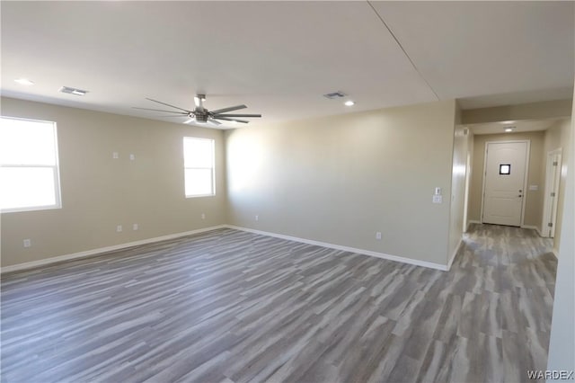 spare room with dark wood-style floors, a ceiling fan, visible vents, and baseboards