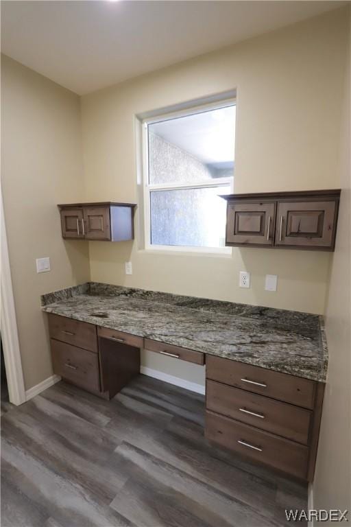 unfurnished office featuring built in desk, dark wood-style flooring, and baseboards