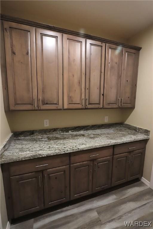 kitchen with light wood-style flooring, dark brown cabinetry, and light stone countertops