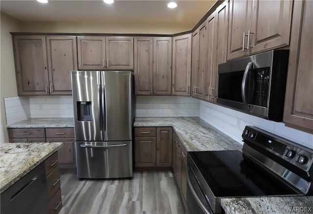 kitchen with stainless steel appliances, light wood-style flooring, dark brown cabinetry, and light stone countertops