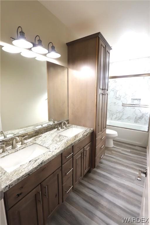 full bath with double vanity, wood finished floors, a sink, and shower / bathing tub combination