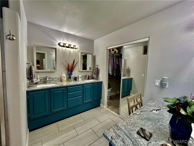 bathroom with a textured wall, a sink, a spacious closet, and double vanity