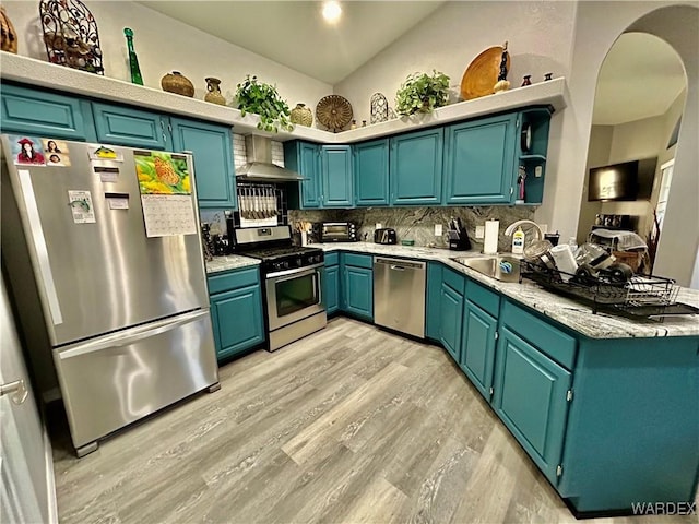 kitchen featuring open shelves, a sink, light countertops, appliances with stainless steel finishes, and wall chimney exhaust hood