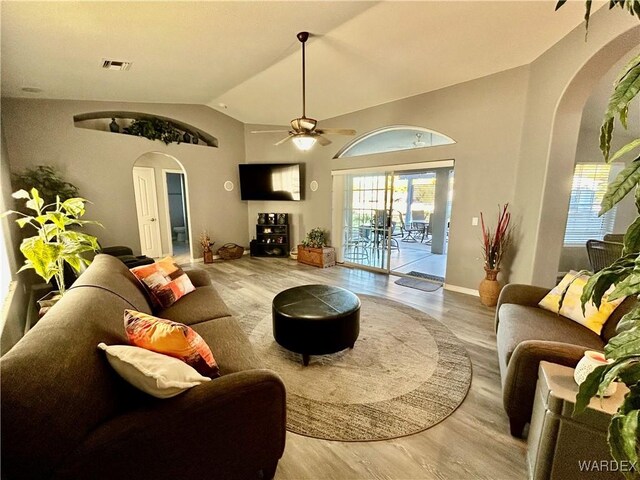 living room featuring arched walkways, lofted ceiling, visible vents, and light wood-style floors