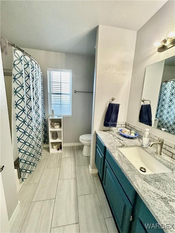 full bathroom featuring toilet, a textured ceiling, vanity, a shower with curtain, and baseboards