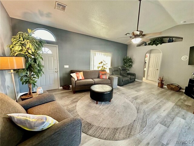 living area featuring lofted ceiling, light wood finished floors, visible vents, and arched walkways